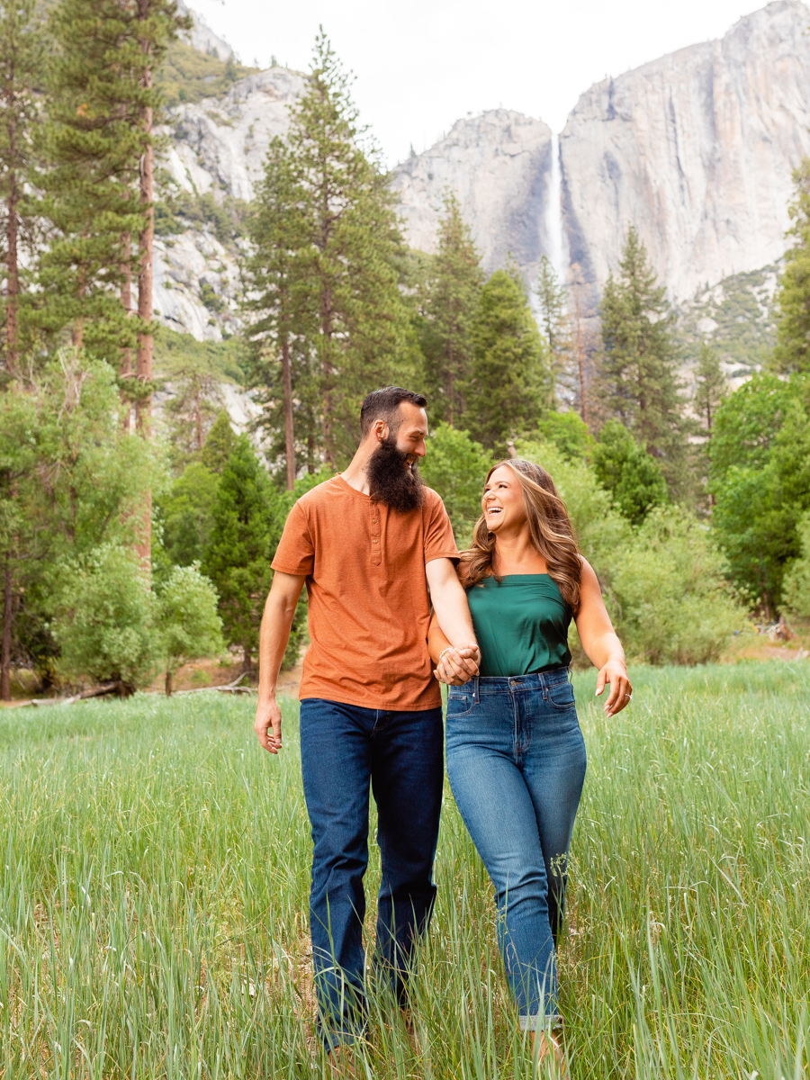 Engaged couple walk through field at Yosemite.