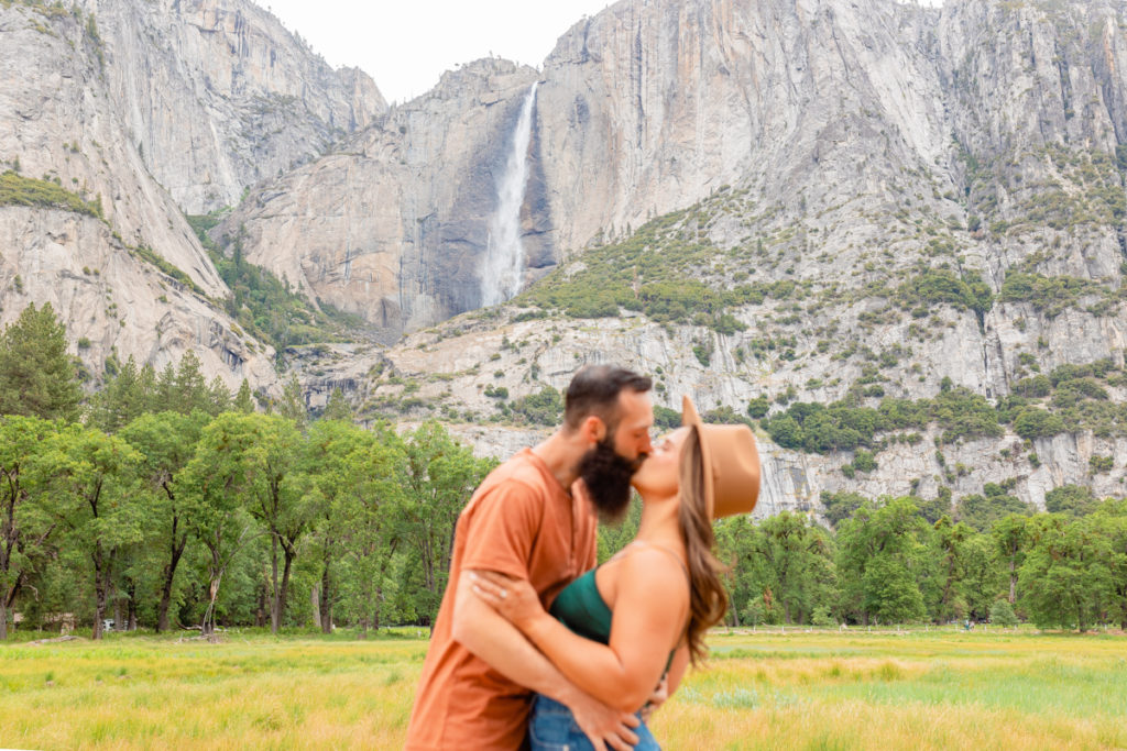 Yosemite falls in focus as engaged couple kiss.